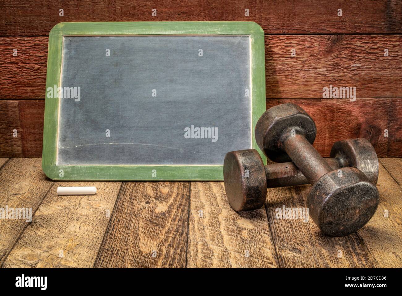 cartello nero in ardesia contro il legno di fienile rustico e stagionato con un paio di manubri, pronto per il testo relativo al fitness, alla dieta o alla perdita di peso Foto Stock
