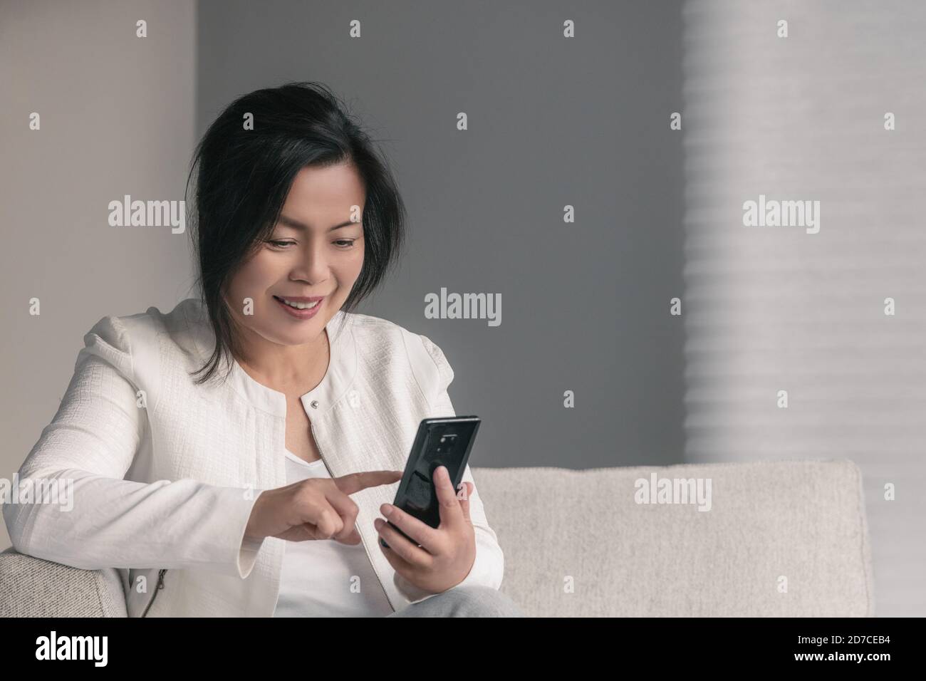 Donna asiatica matura che usa il telefono cellulare durante la casa di distanziamento sociale quarantena sms riunione on-line sul cellulare Foto Stock