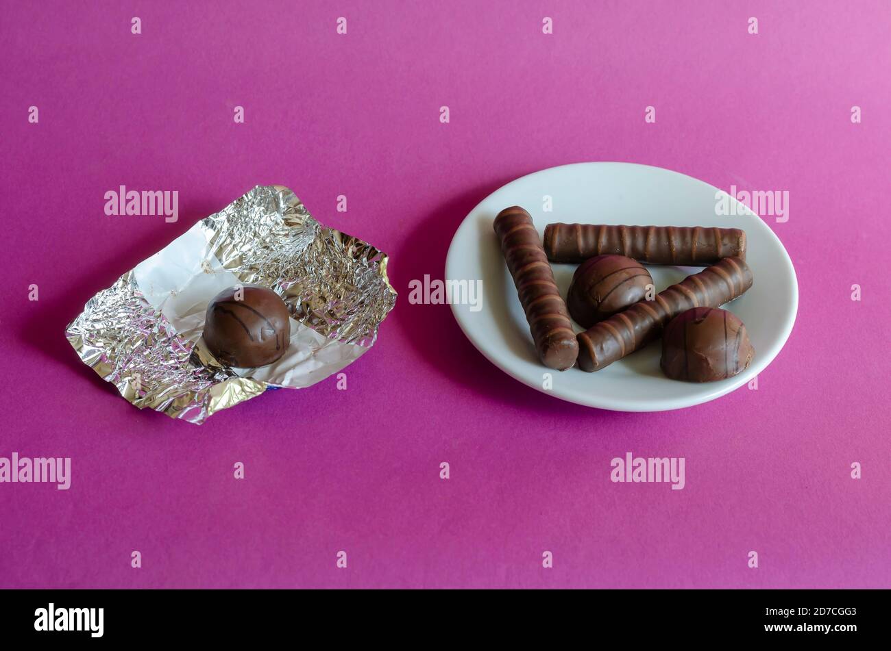 Cioccolatini, piattino bianco e wrapper di caramelle su sfondo rosa. Una porzione di deliziosi dolci pronti. Dolcetti. Foto Stock