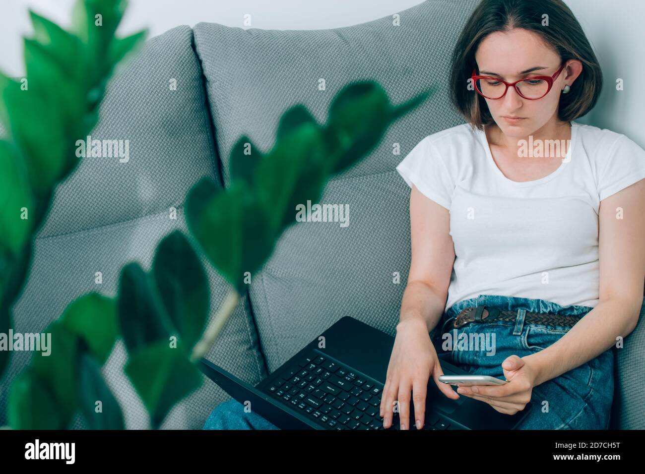 Ritratto di una giovane donna o freelance che lavora da casa in remoto, utilizzando sia il laptop che lo smartphone. Shopping online utilizzando l'app mobile e. Foto Stock