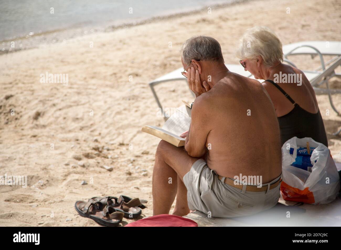 Coppia senior su una spiaggia. Un uomo anziano e una donna che legge e si godono le loro vacanze estive o pensione. Foto Stock