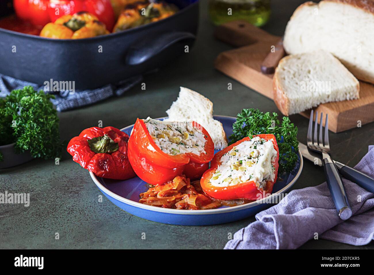 Peperoni dolci farciti al forno con pollo o tacchino, mais ed erbe su piastra in ceramica, fondo verde di cemento. Foto Stock