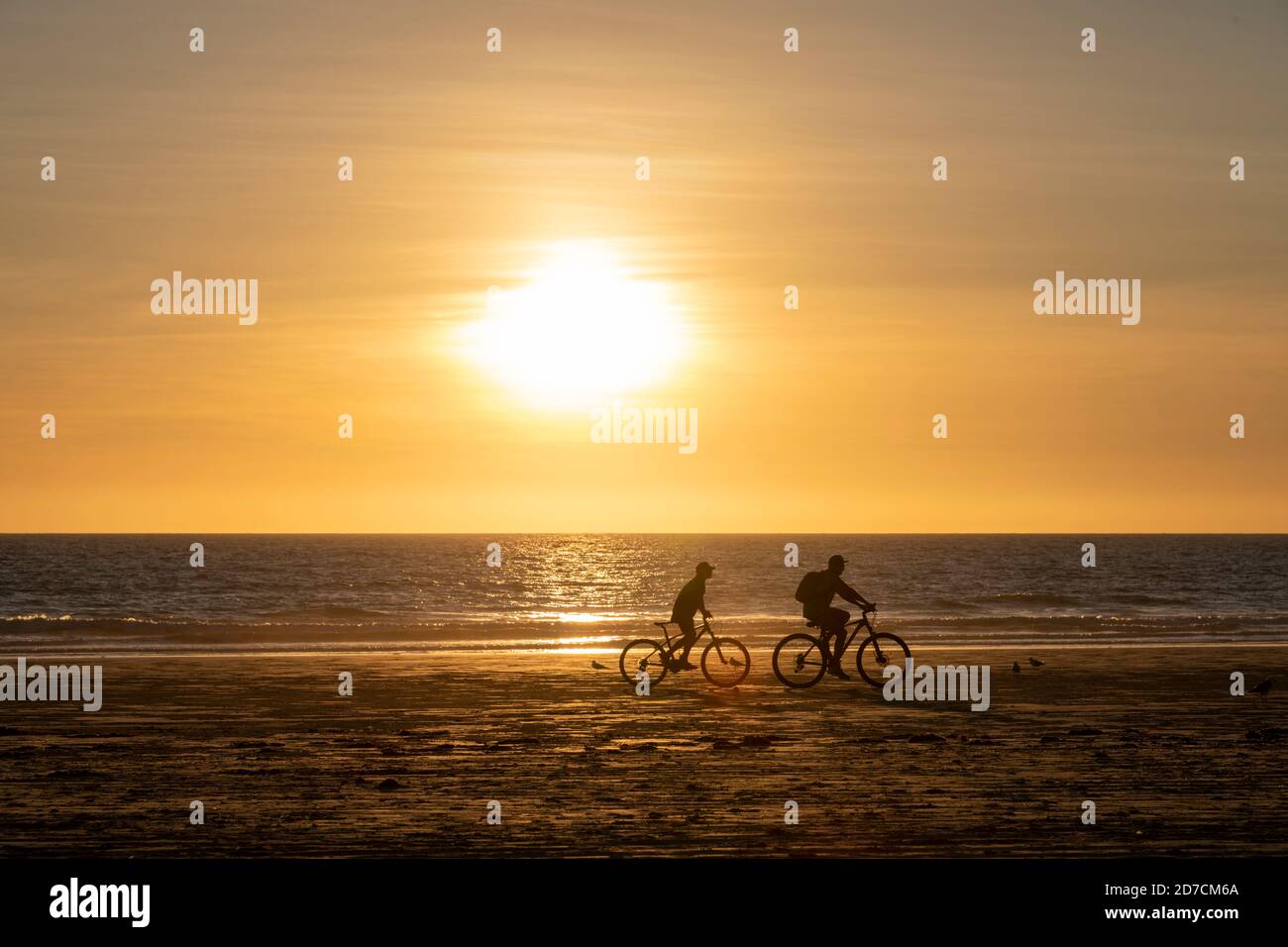 Un padre e un figlio cavalcano le biciclette lungo Cable Beach al tramonto. Foto Stock