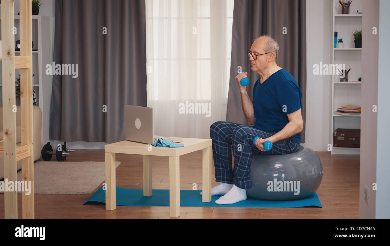 L'uomo anziano che addestra bicipite che guarda la lezione in linea di idoneità. Anziano pensionato sano addestrando sport di salute a casa, esercitandosi attività di idoneità all'età anziana Foto Stock