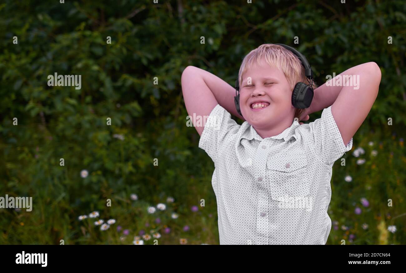 Un ragazzo sorridente con le cuffie e cammina nel Parco in estate Foto Stock