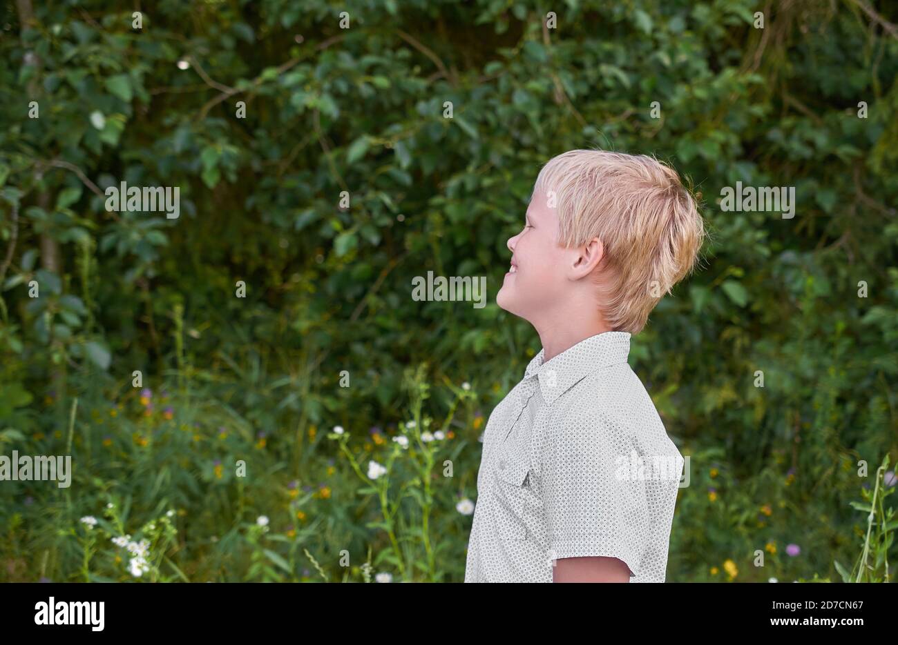 Un ragazzo sorridente in una camicia bianca si trova in un parco in estate. Verticale Foto Stock