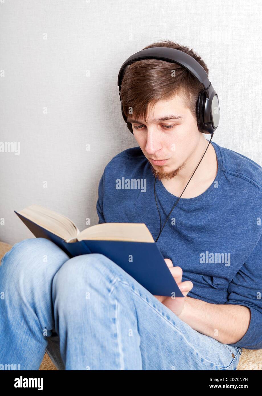 Young Man in Headphones leggere un libro sul divano A casa Foto Stock