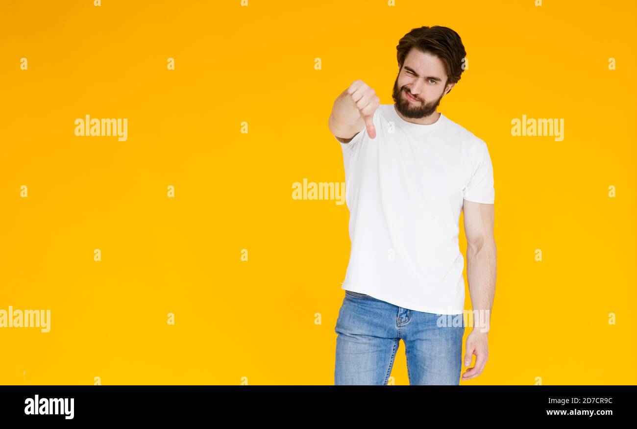 Giovane uomo caucasico isolato su sfondo giallo mostrando il pollice giù ed esprimendo dissimile. Foto Stock