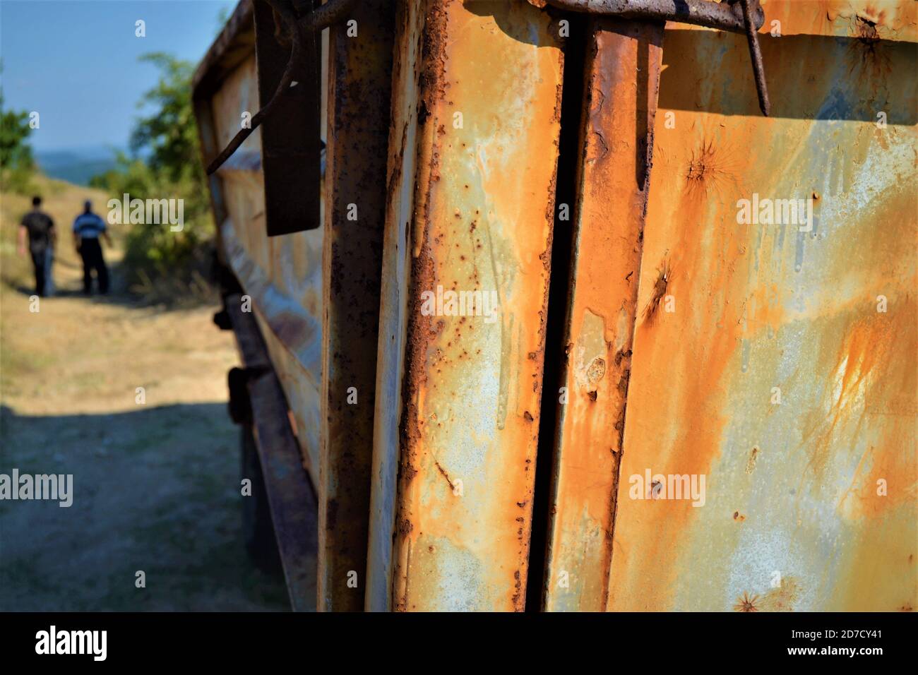 Bulgaria e vista da piccoli e carini villaggi durante il giorno luminoso. Usurato e vecchio un rimorchio del trattore, camminando due uomini e sfondo sfocato. Foto Stock