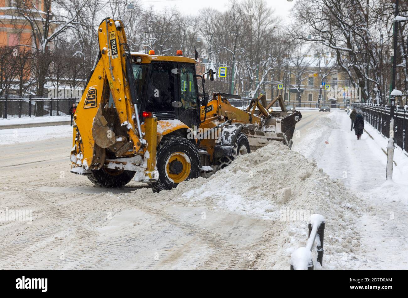 San Pietroburgo, Russia - 06 febbraio 2018: Trattore giallo JCB dopo la caduta di neve libera la strada e la strada in una giornata invernale cupa Foto Stock