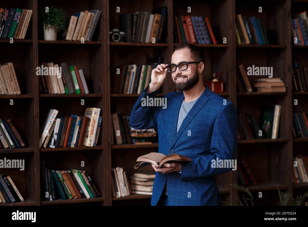 uomo d'affari bearded con gli occhiali in biblioteca con un taccuino in mano sorride. Giovane scrittore Foto Stock