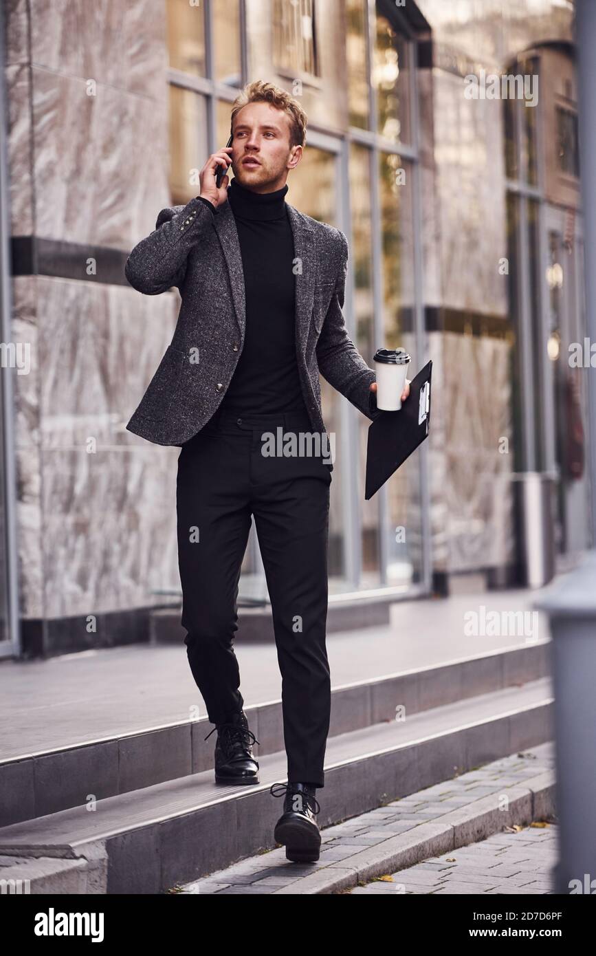 Uomo in elegante abbigliamento formale con una tazza di bevanda e. il  blocco appunti nelle mani e' esterno contro l'edificio moderno  conversazione al telefono Foto stock - Alamy