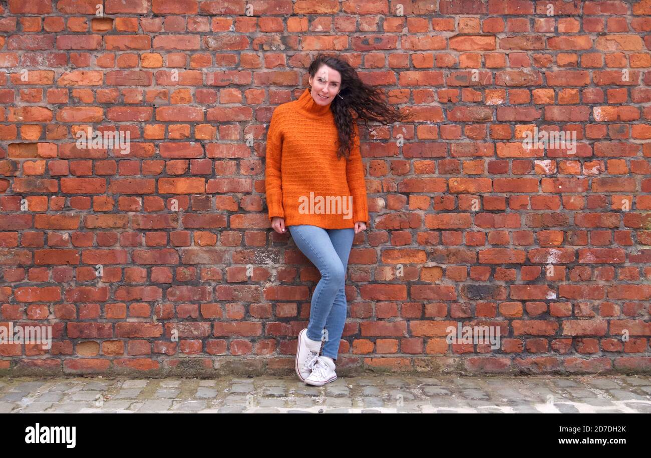 Donna sottile in jumper arancione con capelli soffiati dal vento Foto Stock
