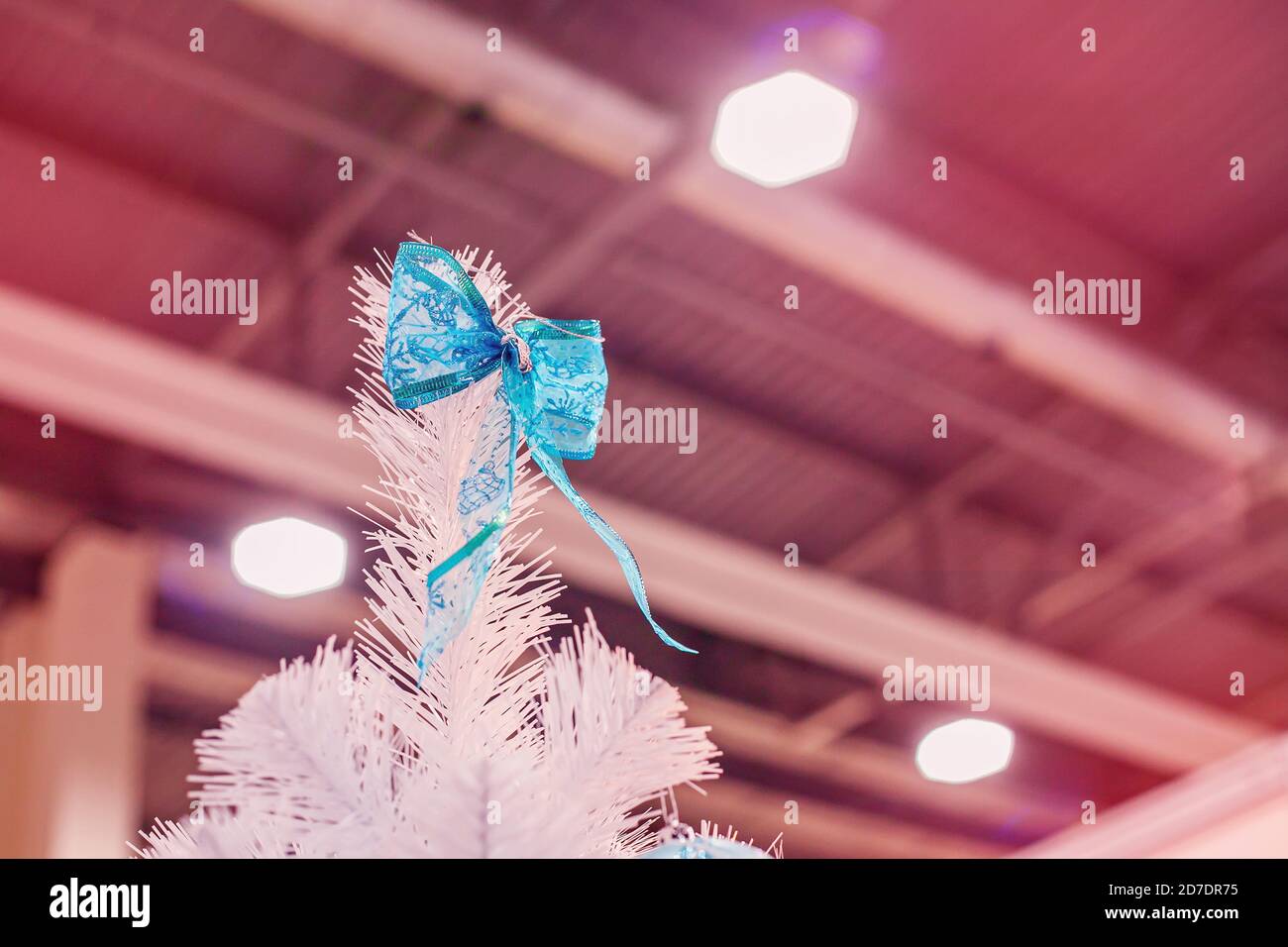 Decorazione di Natale - arco blu appeso sulla cima dell'albero artificiale bianco di Natale alla fiera. Foto Stock