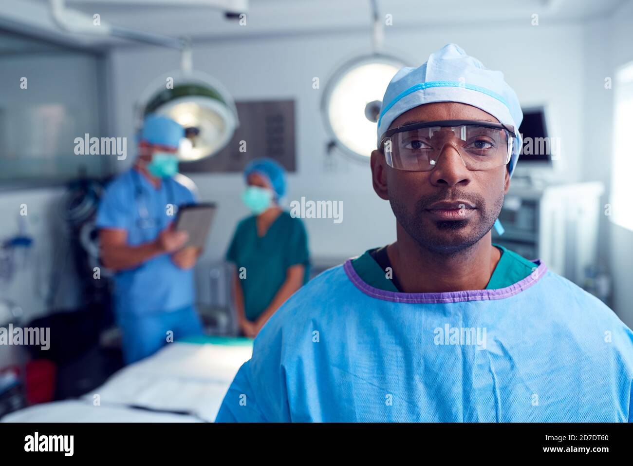 Ritratto del chirurgo maschile che indossa scrub e occhiali protettivi Sala operatoria dell'ospedale Foto Stock