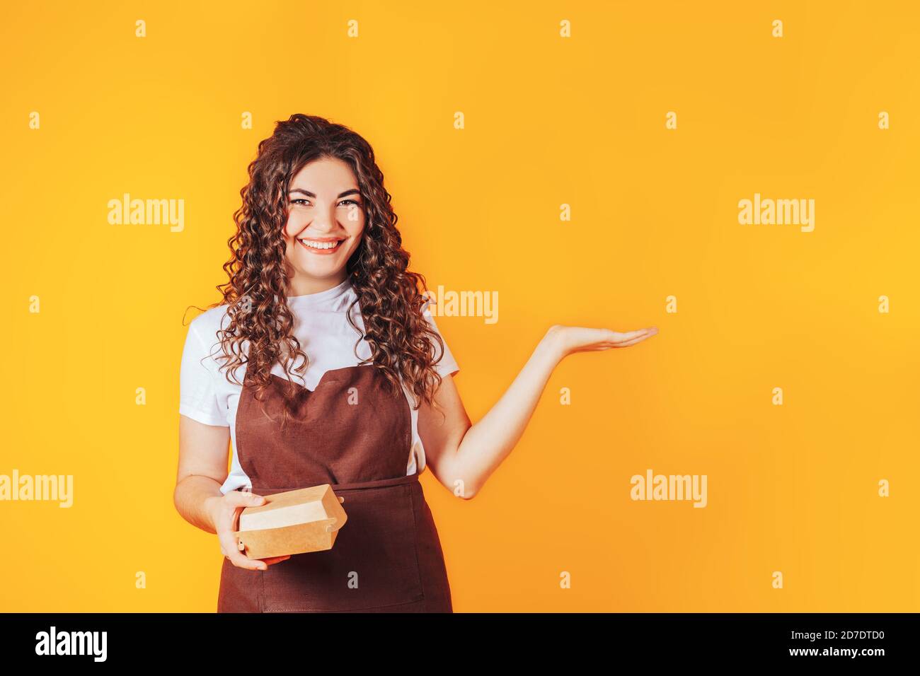 Giovane donna vestita in uniforme da cucina con braccia distese, scatole di cibo in mani Foto Stock