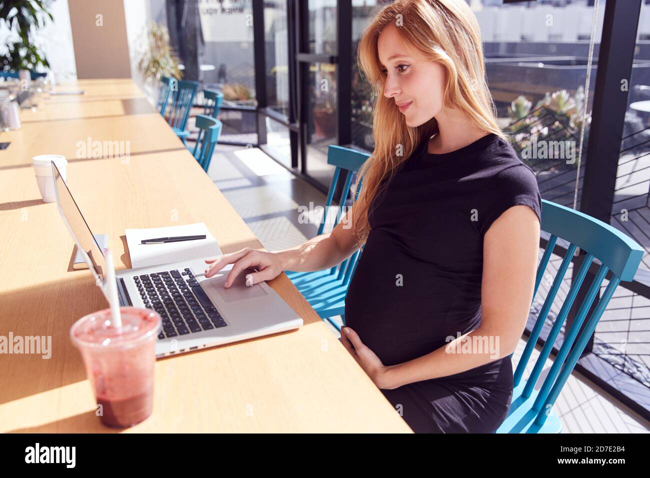 Donna in gravidanza seduto alla scrivania in un ufficio moderno utilizzando un computer portatile Foto Stock