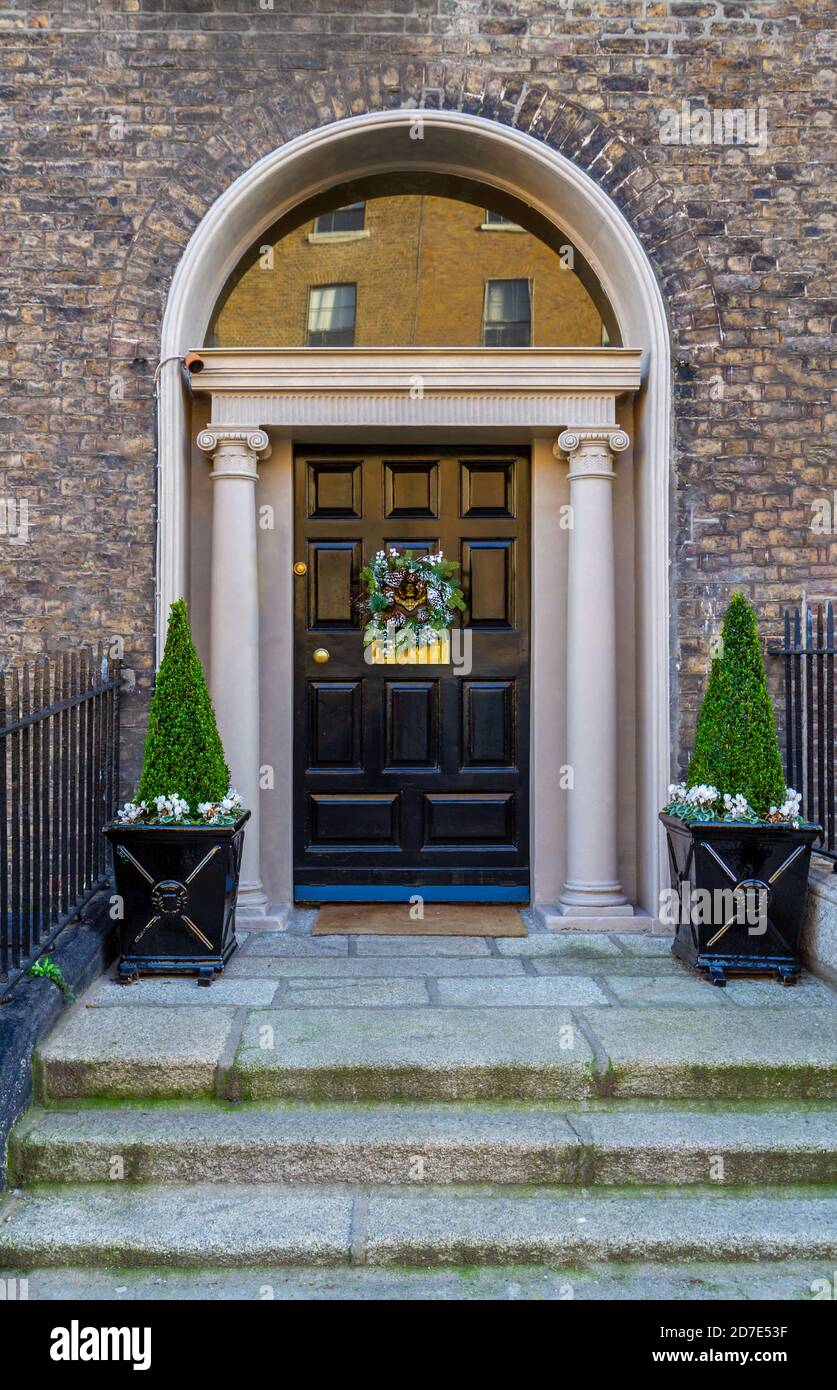 Porta d'ingresso in stile georgiano, decorata per Natale con una corona festiva e due alberi in pentole di piante. Ingresso con colonne in pietra e fanale. Foto Stock