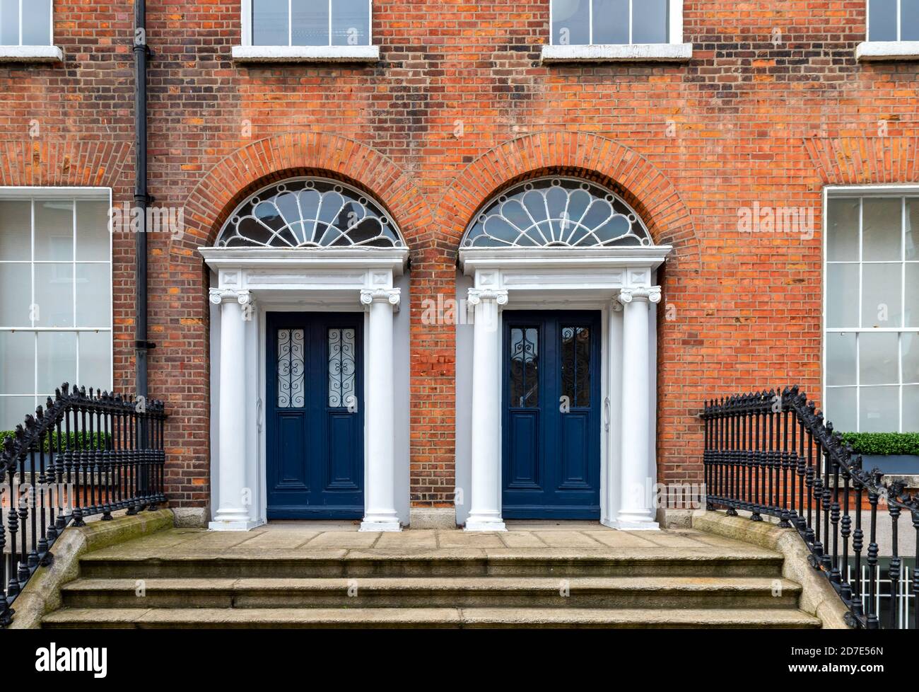 Due porte anteriori blu georgiane con pannelli in vetro, colonne decorative, fanali ad arco, scalini in granito e binari neri. Dublino, Irlanda Foto Stock