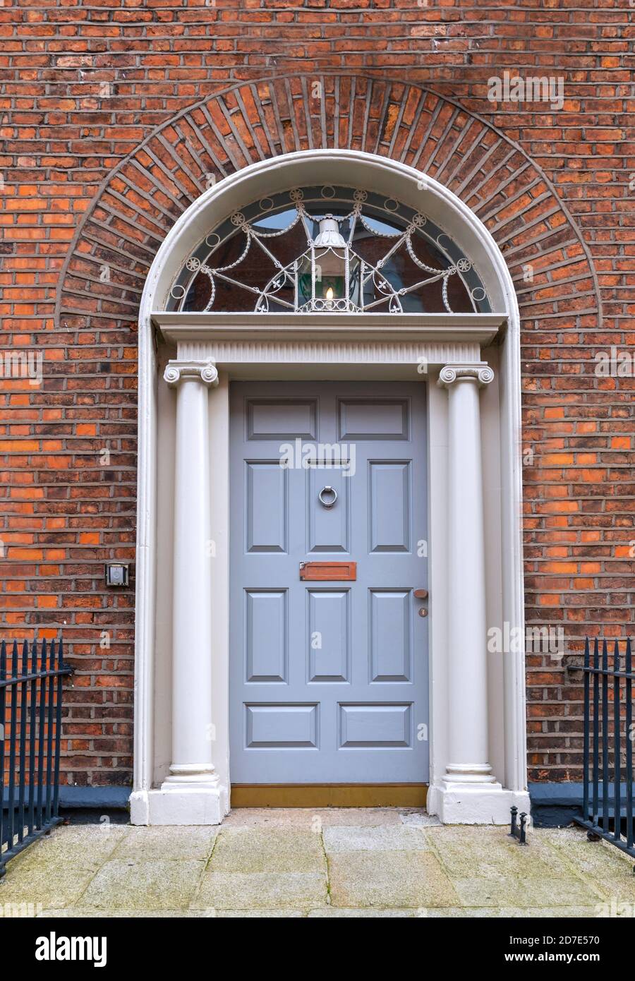 Porta Georgiana grigia, entrata frontale esterna, con faro a ventaglio decorativo, lanterna e colonne in pietra in un vecchio edificio di mattoni rossi. Dublino, Irlanda Foto Stock