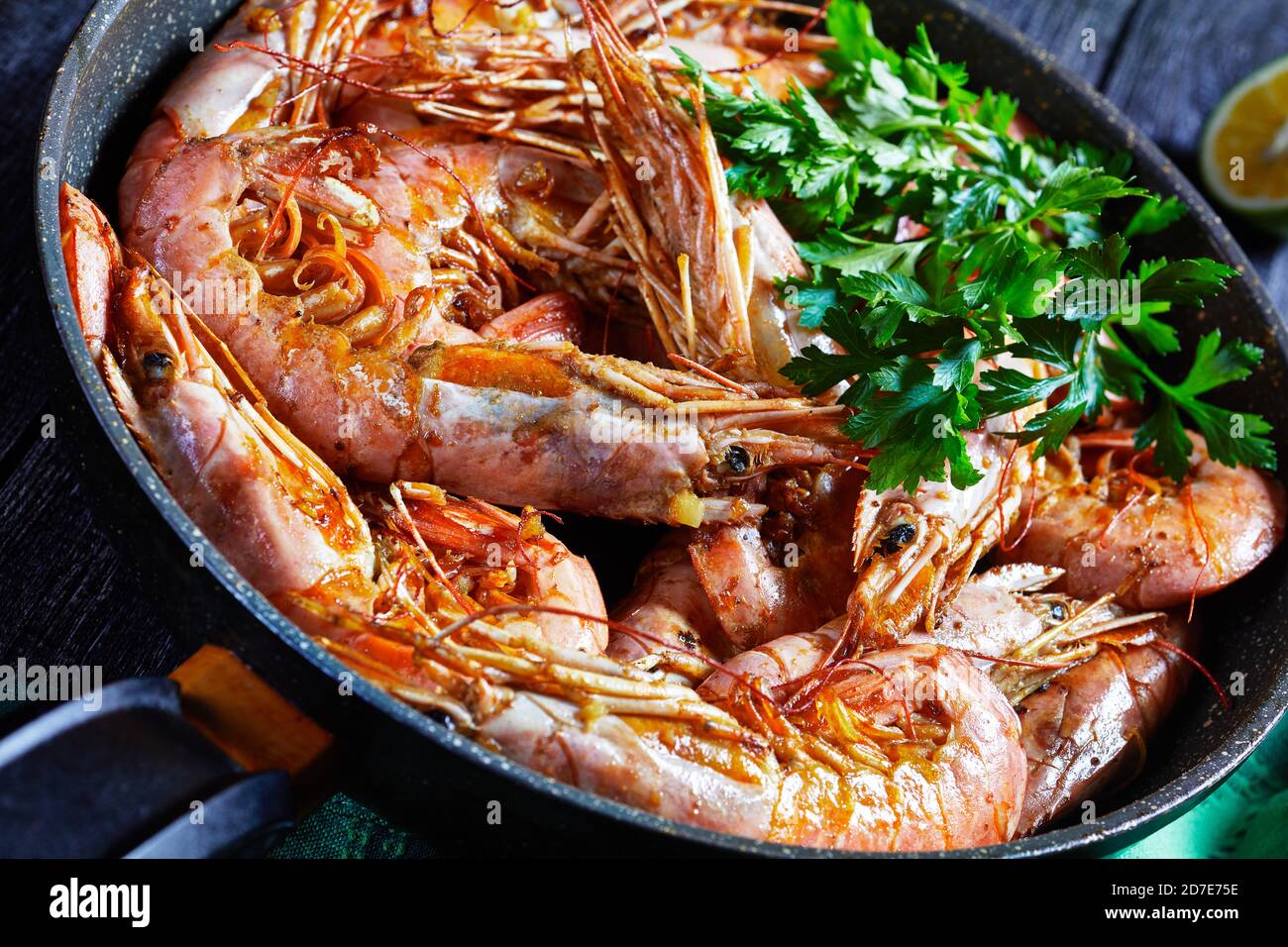 Gamberetti al burro all'aglio cucinati su una padella con lime e prezzemolo fresco di gamberi o gamberi di grandi dimensioni serviti su sfondo di legno, vista dall'alto, primo piano Foto Stock