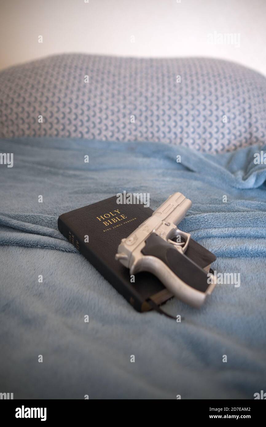 una replica argento berretta 9 mm pistola su una pelle nera La Sacra Bibbia poggia su un letto fatto in una camera da letto a casa di alcuni Foto Stock