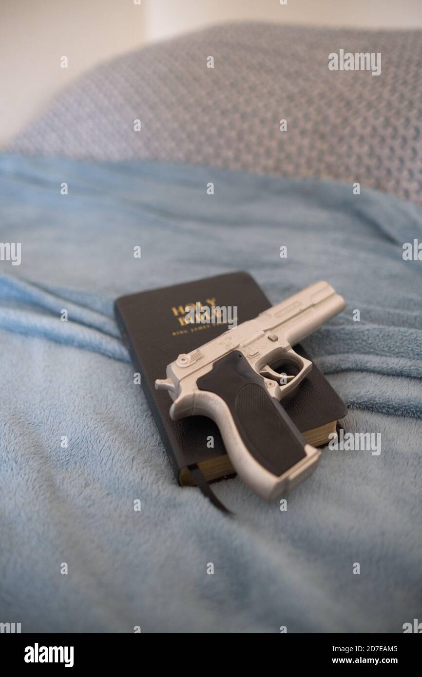 una replica argento berretta 9 mm pistola su una pelle nera La Sacra Bibbia poggia su un letto fatto in una camera da letto a casa di alcuni Foto Stock