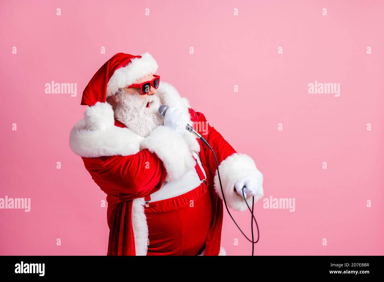 Profilo foto laterale di bianco grigio barba capelli funky pazzo babbo natale look copyspace cantare microfono x-mas canzoni di natale indossare sospenditori di usura della testa del cappuccio Foto Stock
