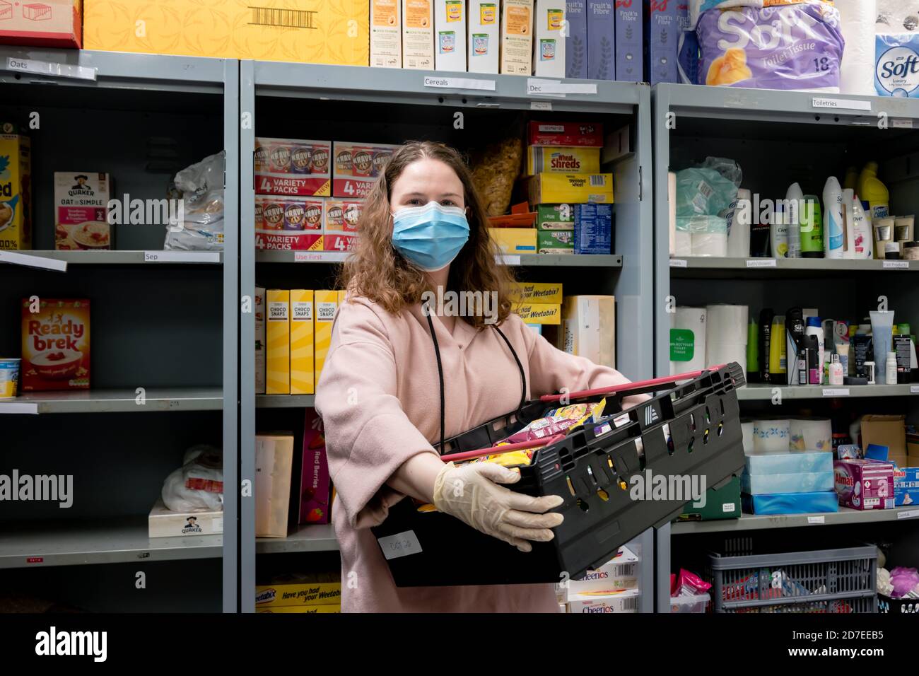 Un volontario presso una banca alimentare Trussell Trust indossa guanti I PPE nella pandemia del coronovirus mentre imballano un pacchetto del cliente Foto Stock