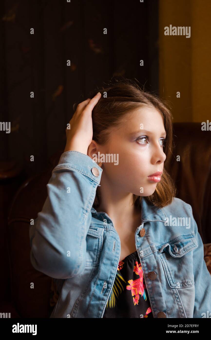 Un ritratto naturale di una ragazza teen o tween con la mano e le dita che corrono attraverso i capelli seduti in una poltrona, guardando pensieroso Foto Stock