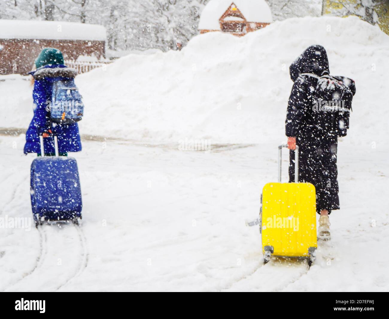Le ragazze con zaini e valigie camminano lungo la strada innevata durante le forti nevicate. L'immagine è fuori fuoco. Effetto immagine sfocata Foto Stock