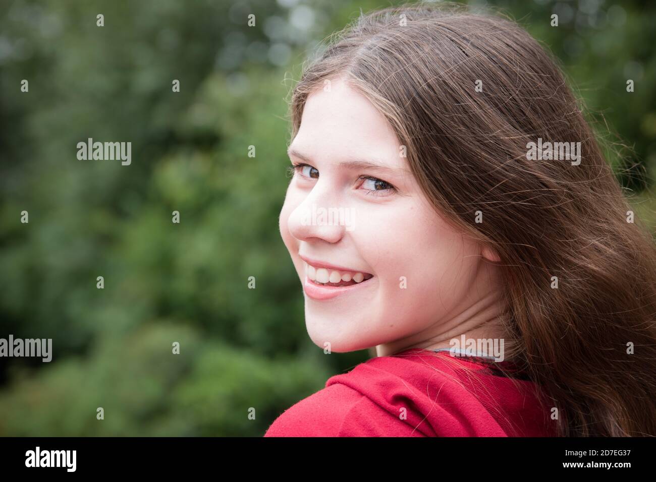 Bel ritratto naturale della ragazza adolescente con lunghi capelli marroni guardando indietro la fotocamera con il sorriso che mostra i denti Foto Stock