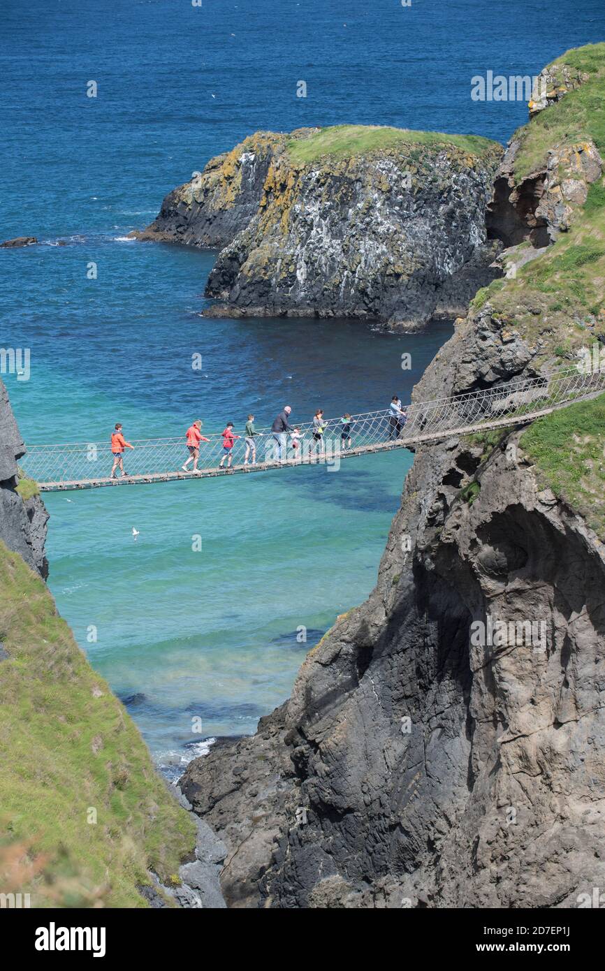 I turisti attraversano il ponte di corda Carrick-a-Rede, un ponte sospeso sulla costa di Antrim, nell'Irlanda del Nord, Regno Unito Foto Stock
