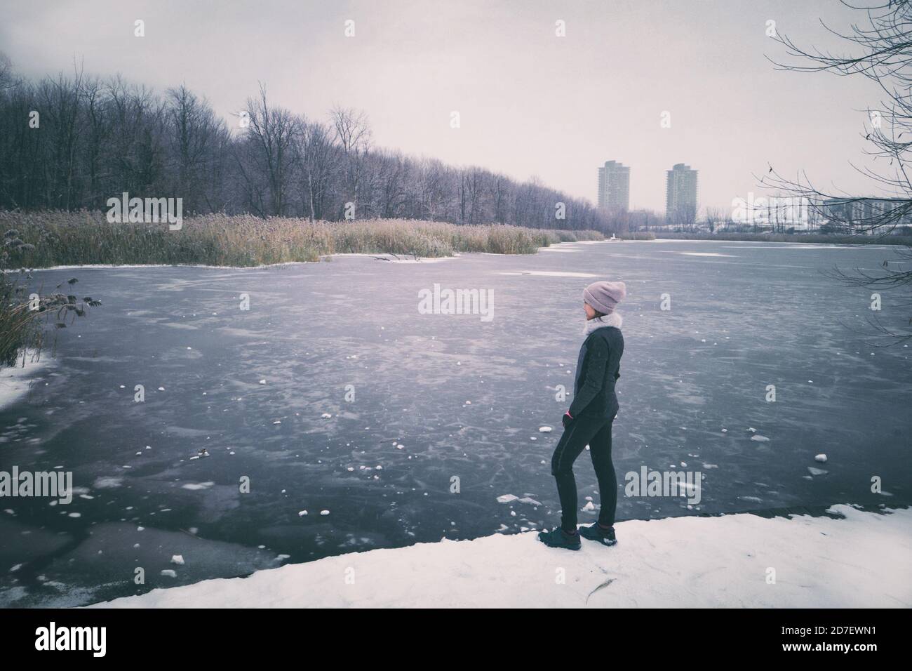 Inverno natura paesaggio percorso pista corridore donna facendo una pausa al lago ghiacciato godendo scenario di freddo inverno vista. Sfondo del parco cittadino Foto Stock