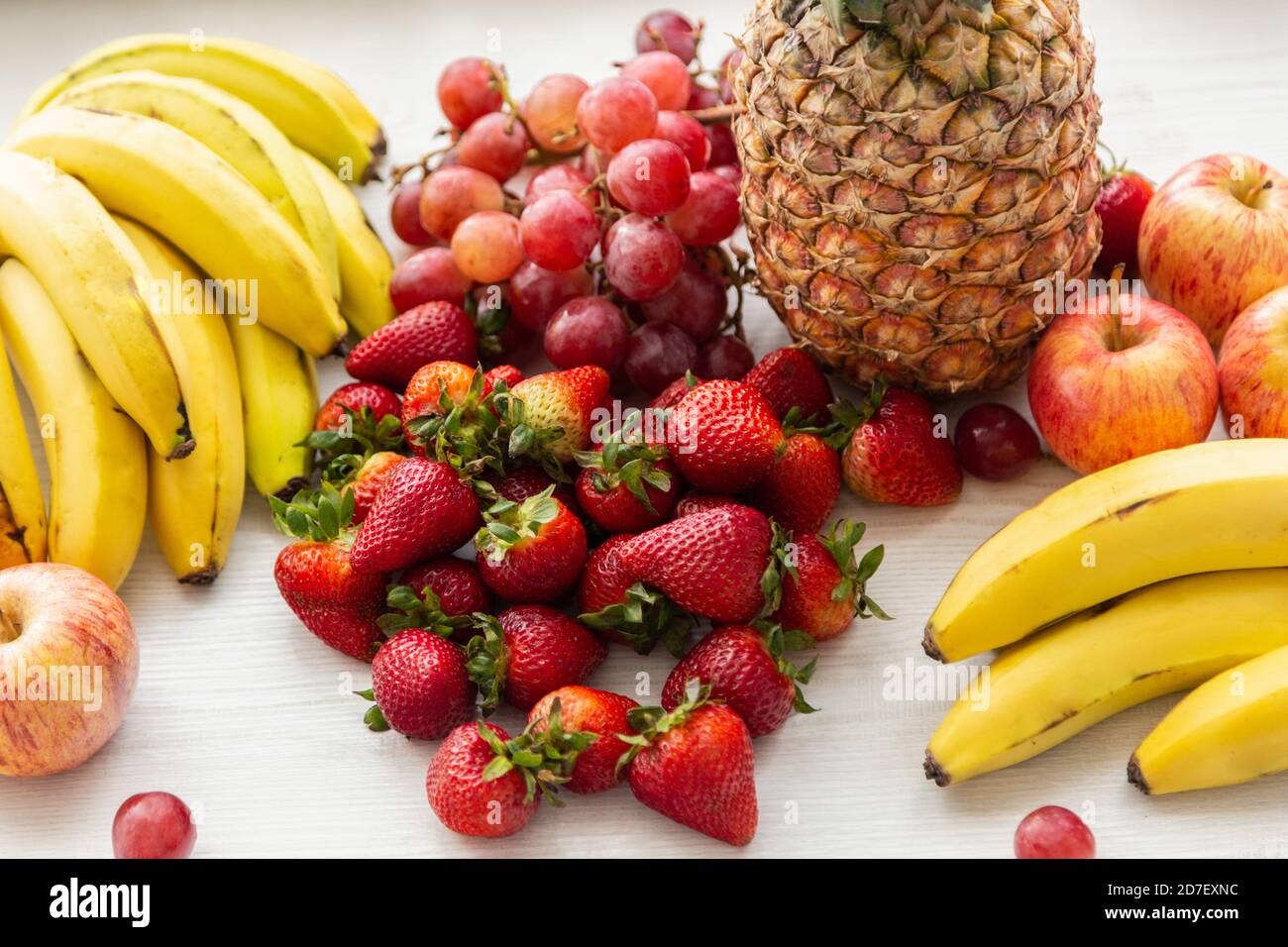 primo piano di deliziosa frutta fresca su sfondo bianco, ananas, banane, mela, fragola, uva e banane, stile di vita sano, studio Foto Stock