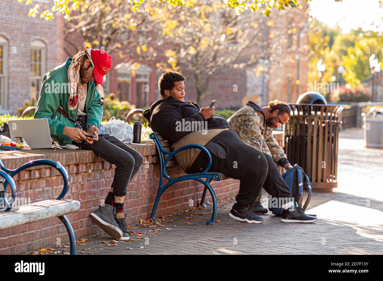 Frederick, MD, USA 10/14/2020: Un gruppo di poveri che vivono per strada è seduto su una panchina con i loro beni in zaini. Guardano la loro mobil Foto Stock