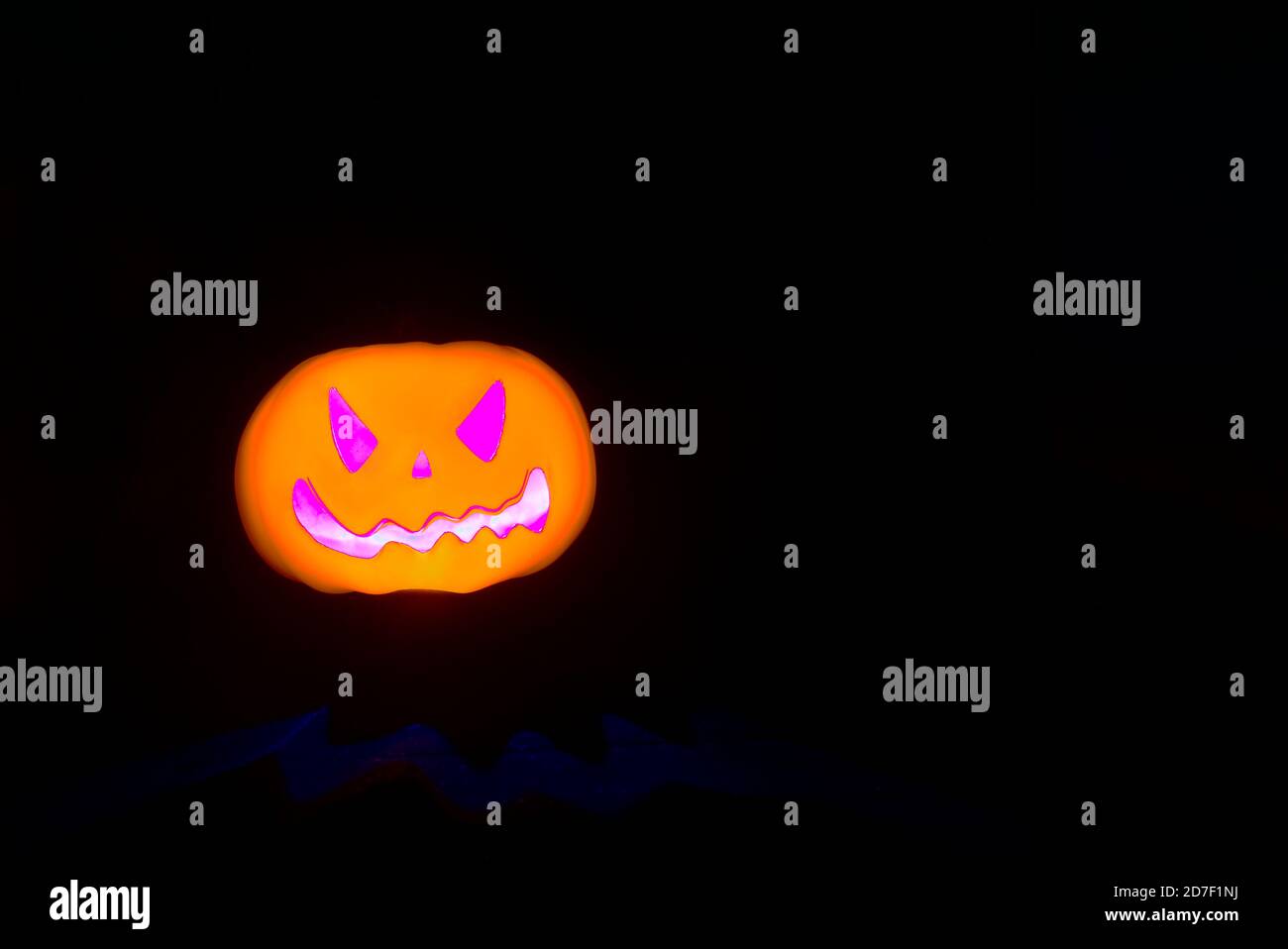 Zucca di Halloween gialla spaventosa con bocca incandescente viola e gli occhi si illuminano su sfondo nero e con spazio di copia. Zucca che brilla al buio Foto Stock