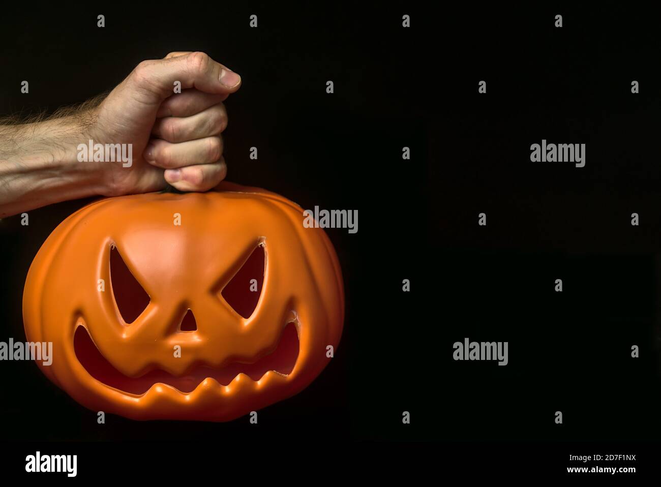 Mano dell'uomo che tiene sullo stelo della zucca. Tema spaventoso di Halloween 2020. Bella mano maschile mantenendo isolata zucca incandescente su sfondo nero. Spazio di copia Foto Stock
