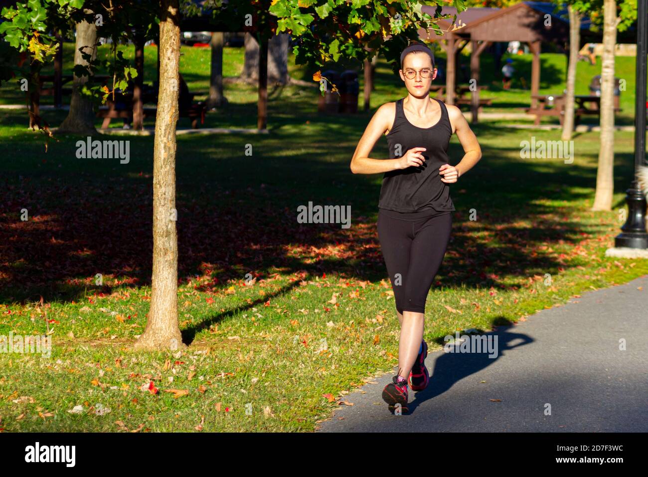 Frederick, MD, USA 10/14/2020: Una giovane donna caucasica con archetto e occhiali, con un canotta nera e collant, fa jogging da sola su asfalti Foto Stock
