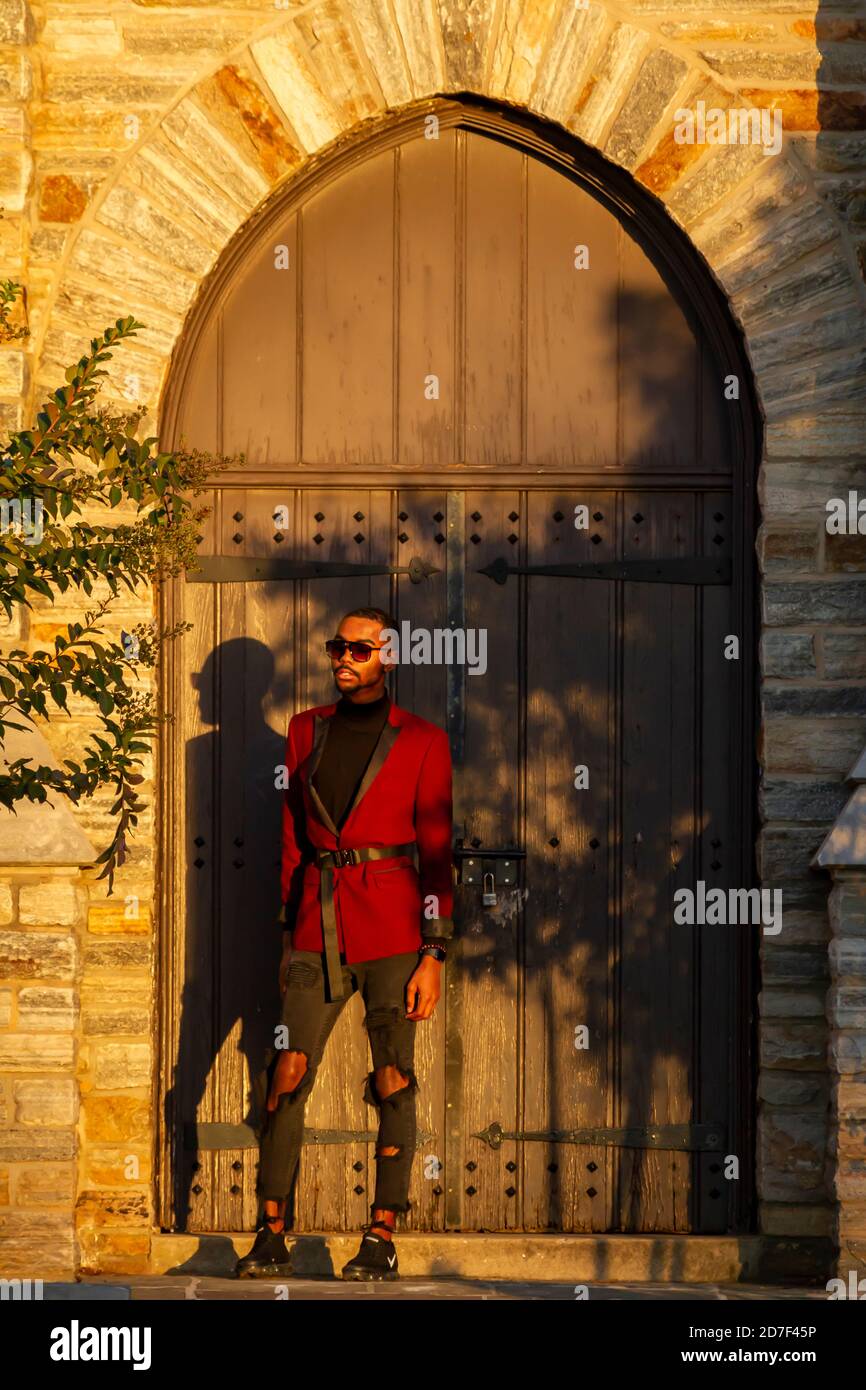 Frederick, MD, USA 10/14/2020: Modello maschile afroamericano che indossa giacca rossa alla moda, occhiali da sole e jeans strappati posa in un luogo storico WIT Foto Stock