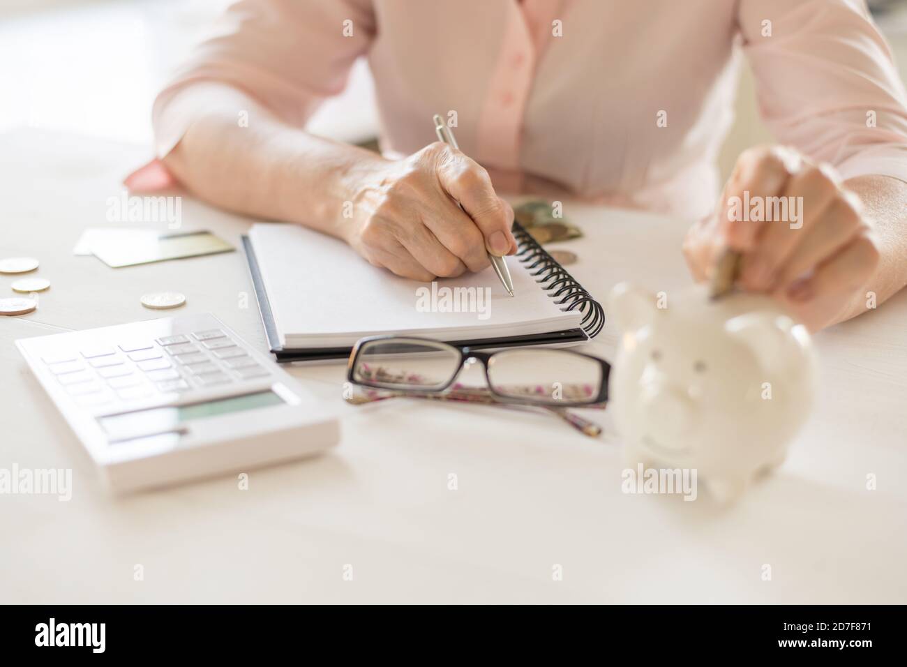Le mani delle donne anziane mettono le monete di denaro in una banca piggy, il concetto di pensionamento, risparmio, vecchiaia. Foto Stock
