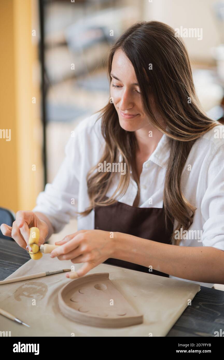Donna che lavora con l'argilla con le mani e l'utensile da taglio ad anello da vicino in un laboratorio di ceramica. Foto Stock