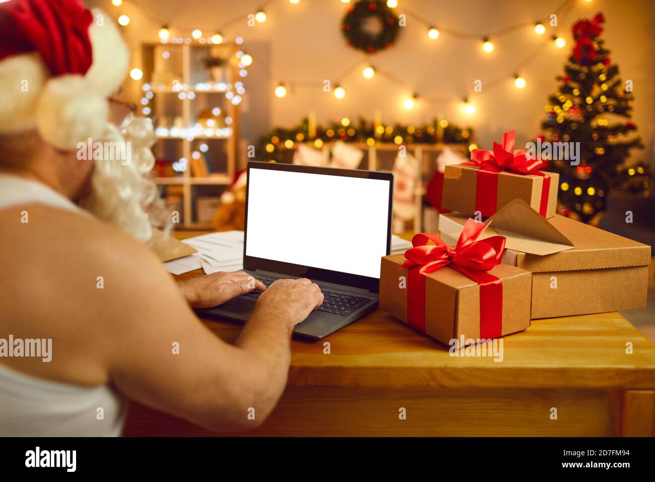 Babbo Natale che lavora su un computer portatile con schermo vuoto seduto a. scrivania nel comfort di casa sua Foto Stock