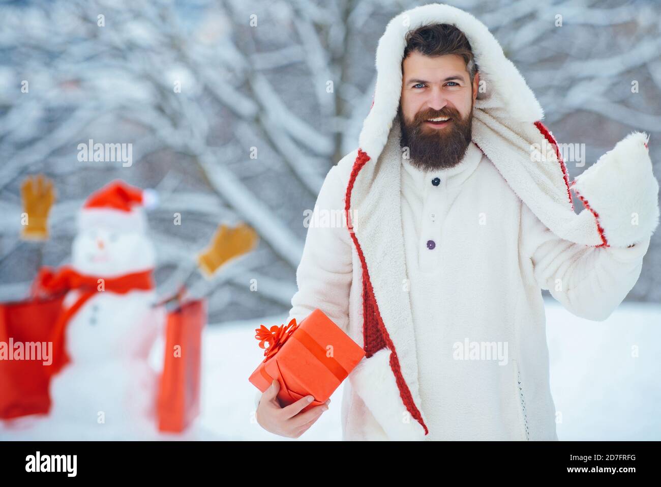 Divertente uomo Santa in posa con scatola regalo rossa in inverno. Gioioso Padre tenere dono e divertirsi con lo snowman in Winter Park. Foto Stock