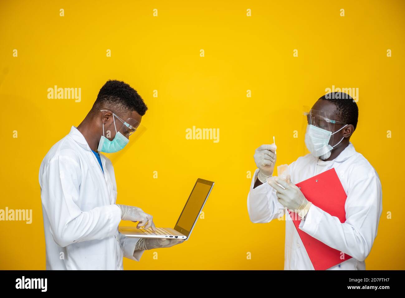 due giovani scienziati africani che indossano camici da laboratorio e maschere facciali e scudi che svolgono uno studio, con computer portatile Foto Stock