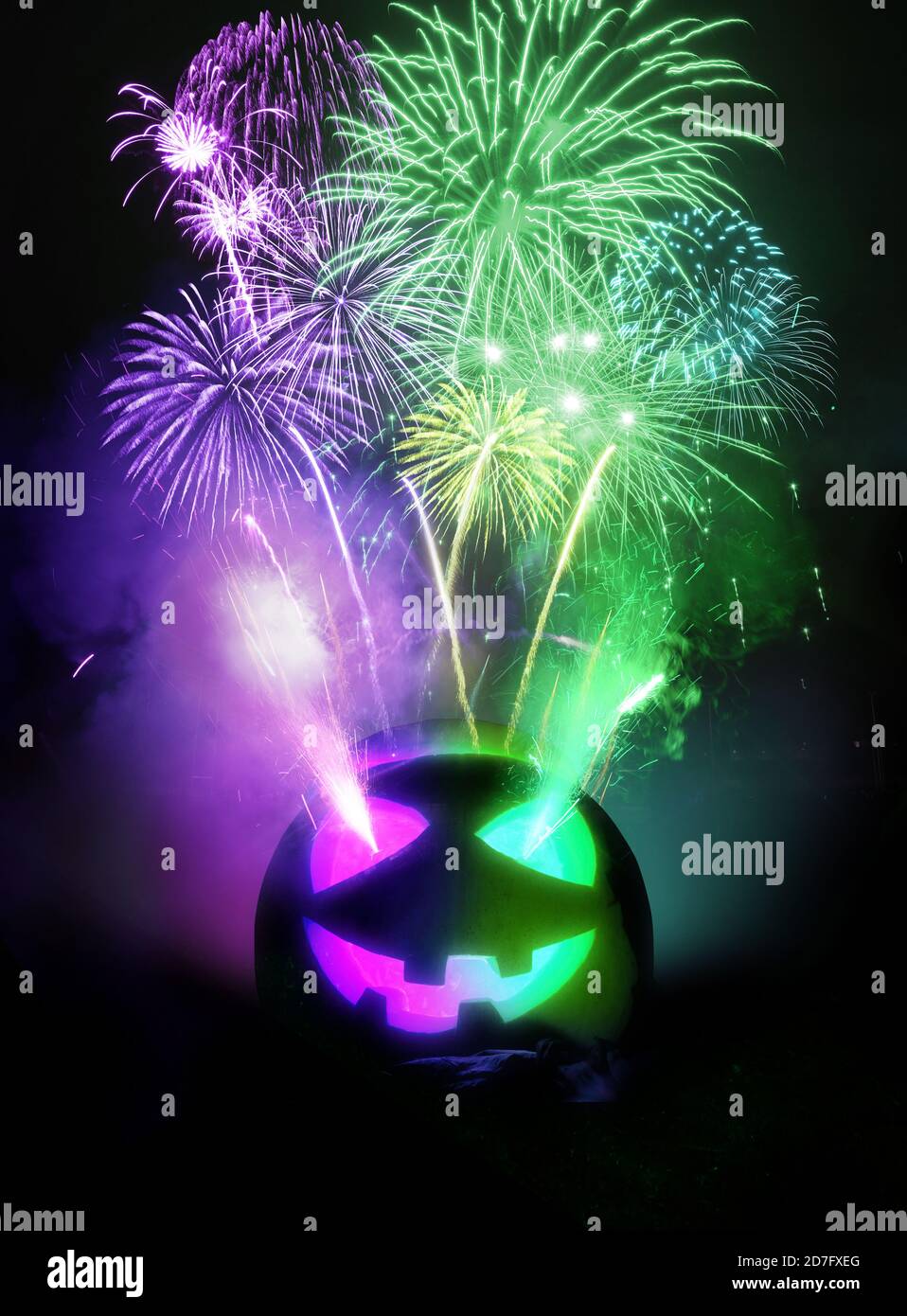 Sfondo della festa di Halloween. Un jack o lanterna scolpito zucca che illumina viola e verde con fuochi d'artificio in fase di rilascio nel cielo notturno. Foto composito Foto Stock