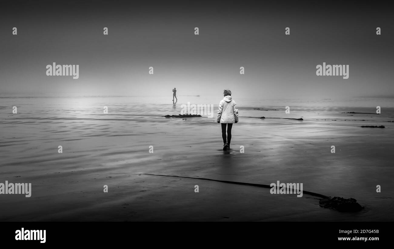 Foto in bianco e nero di una donna che cammina nella fitta nebbia sulla Sandy Beach a Cox Bay presso il Pacific Rim National Park sull'isola di Vancouver, British Columbia Foto Stock