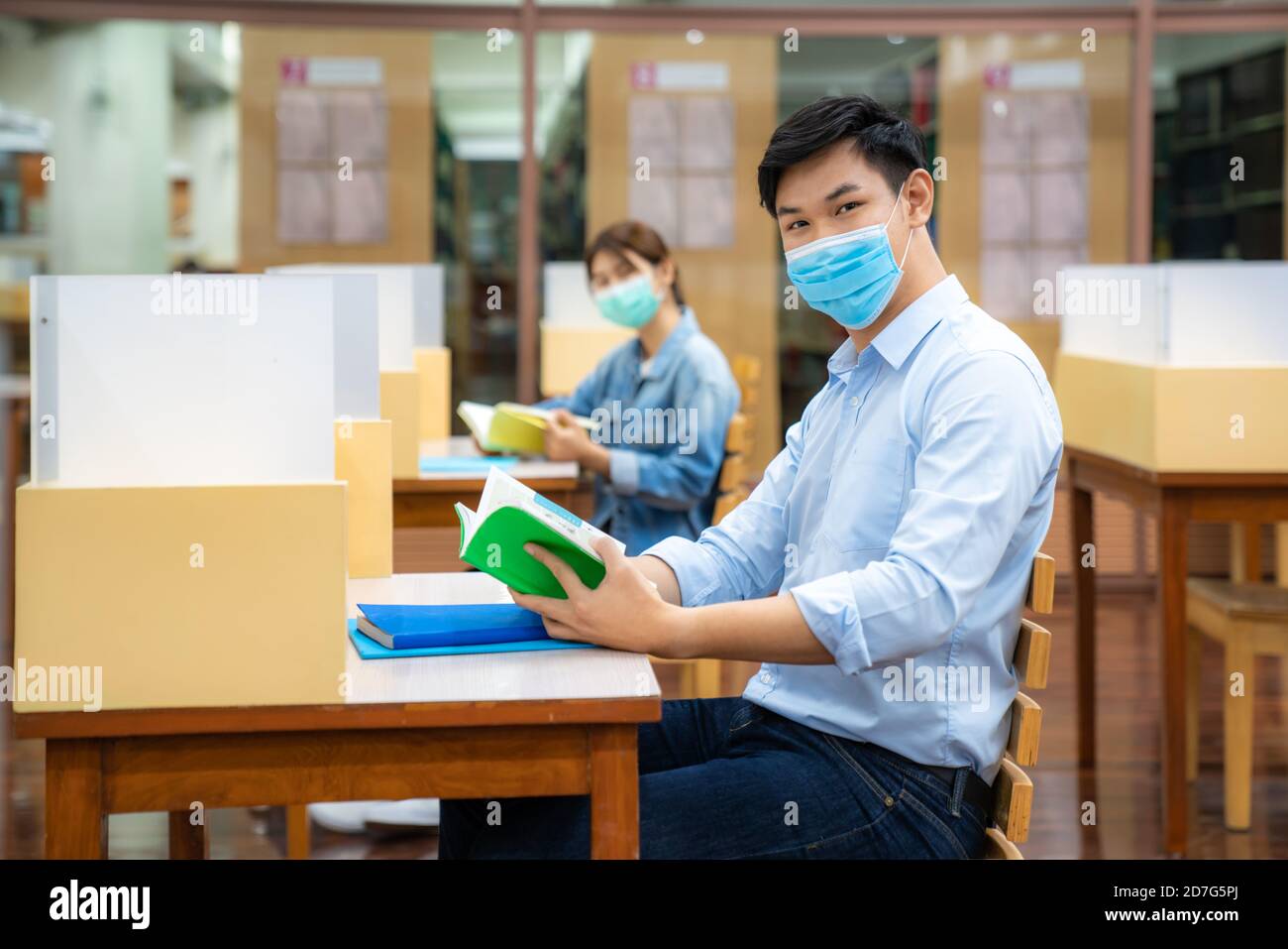 Due studenti universitari asiatici indossando maschera e seduta e. sorridi nella distanza sociale della biblioteca da altri 6 feets a. evitare la diffusione del coronavirus Foto Stock