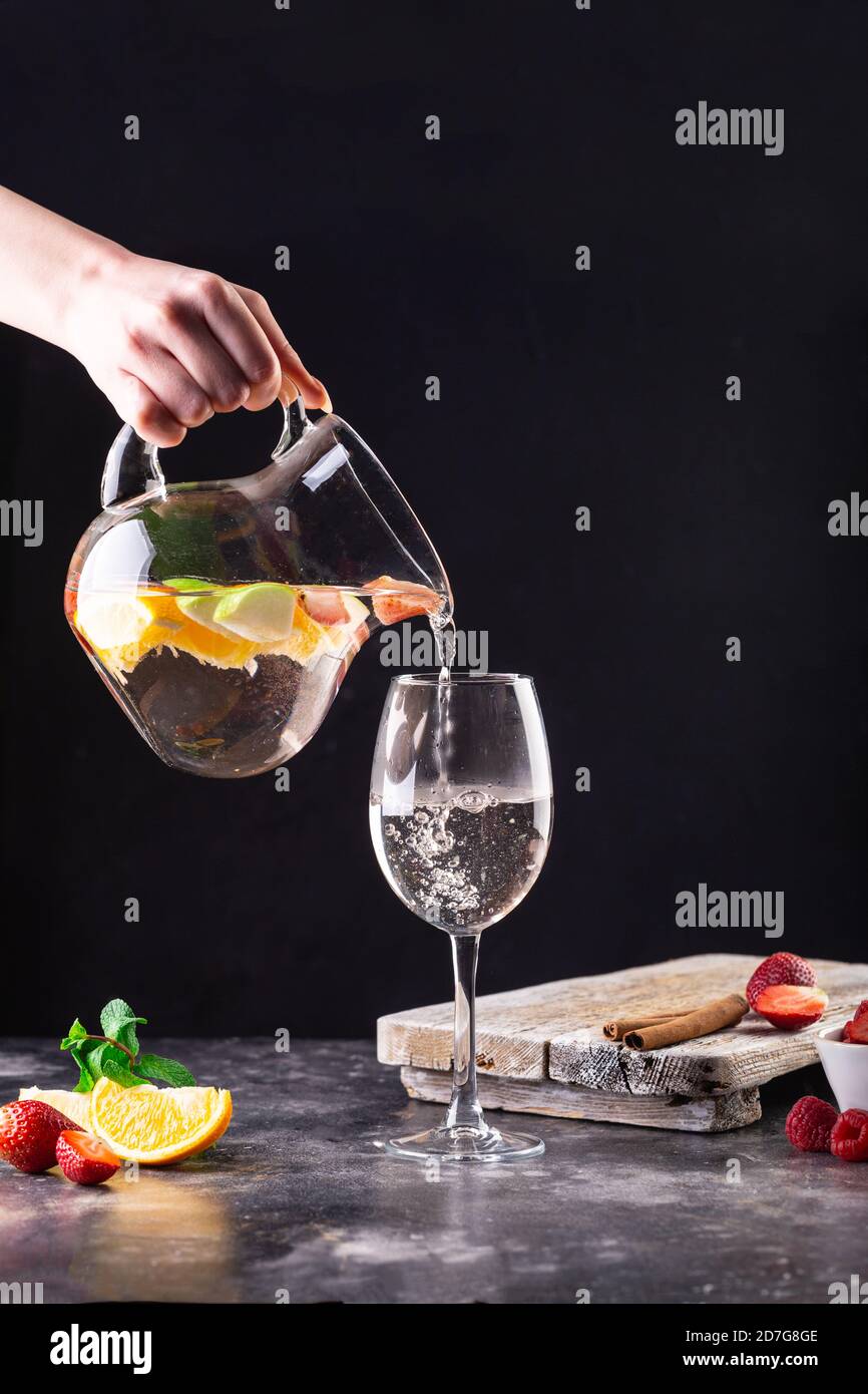 La ragazza che tiene in mano un decanter versa una limonata fresca in un bicchiere. Sul tavolo si trova un cuneo di arancia, fragole, lamponi, una cannella Foto Stock