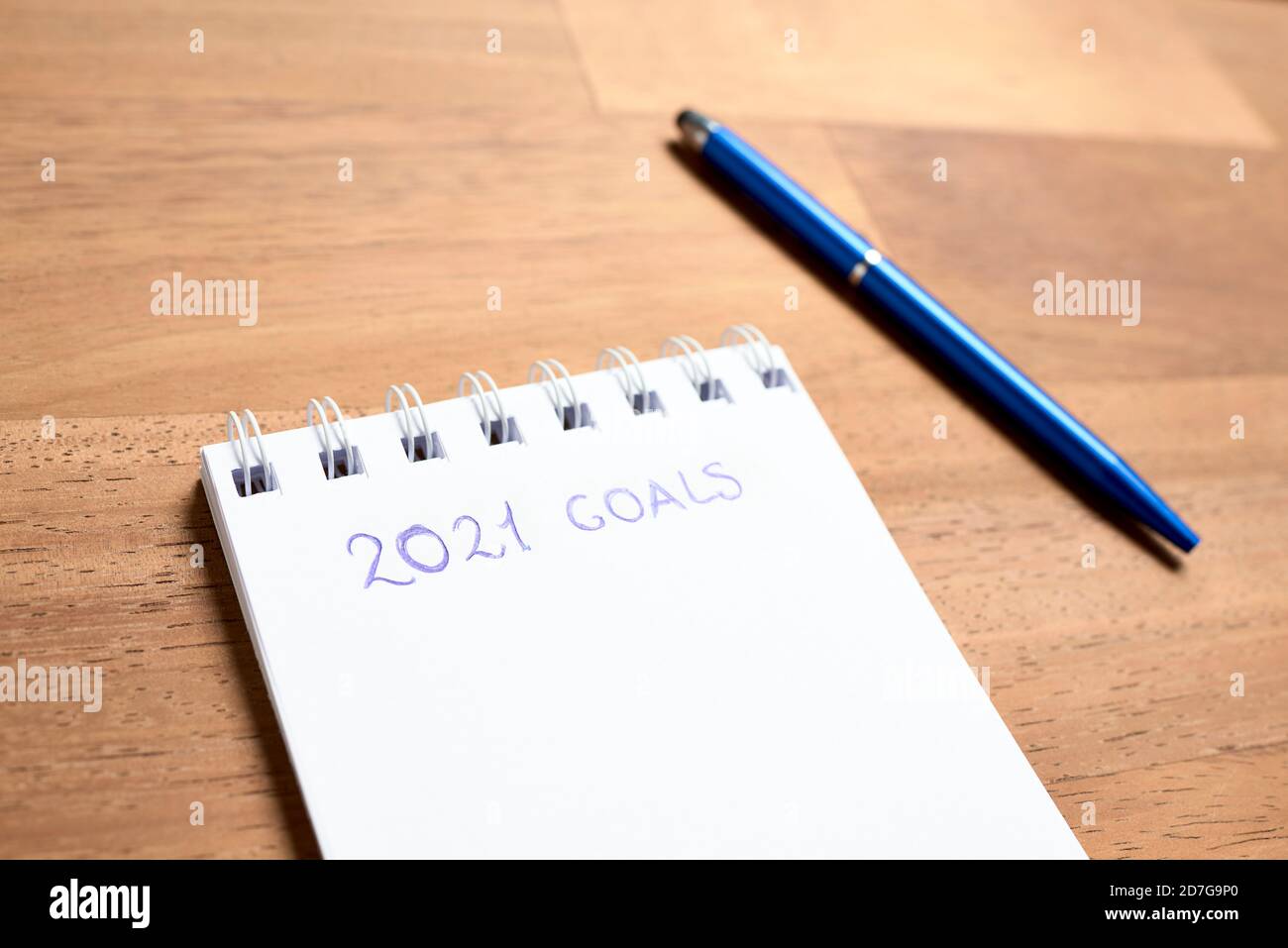 Pagina vuota di un taccuino per annotare gli obiettivi per il nuovo anno 2021 e una penna blu, su una scrivania in legno, con spazio per la copia Foto Stock